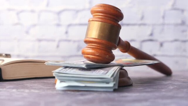 Wooden gavel resting on stack of hundred dollar bills with law book and handcuffs in background