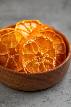 Dehydrated orange citrus fruit slices in round rustic wooden bowl on grey textured stone table