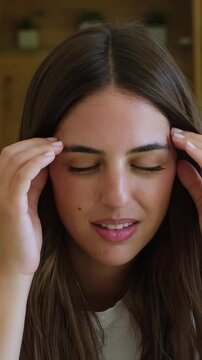 Young stressed woman suffering from a painful headache, massaging her temples with her eyes closed, feeling unwell and exhausted due to a migraine attack and emotional stress