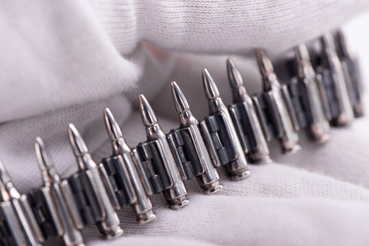 A close-up photo of a silver bracelet designed to look like a machine-gun belt. Rifle Bullet Ammunition Belt Close Up in hand wearing white textile glove