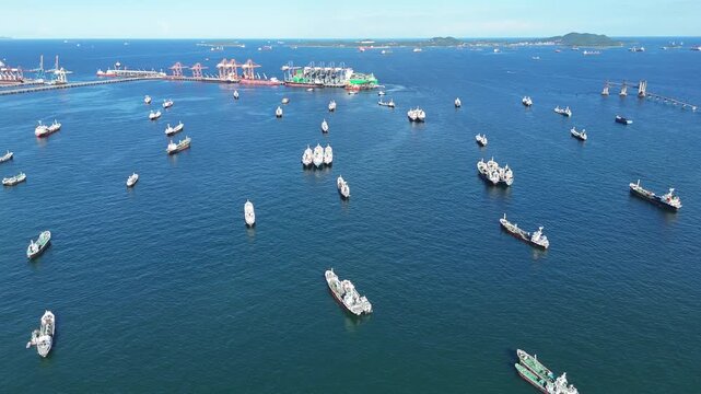Fleet of oil tanker ships and commercial cargo vessels anchored in the deep blue sea near a long bridge. Global maritime logistics, international shipping trade, and energy transport.	