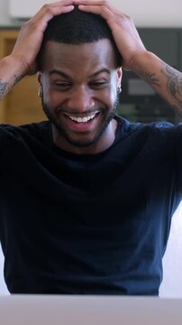 Young black man feeling overjoyed and excited, celebrating a victory or good news while looking at his laptop screen. Triumphant person expressing happiness after winning an online competition