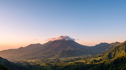 Obraz premium Mountain peak capped with a single cloud stands over a lush green valley at sunrise.