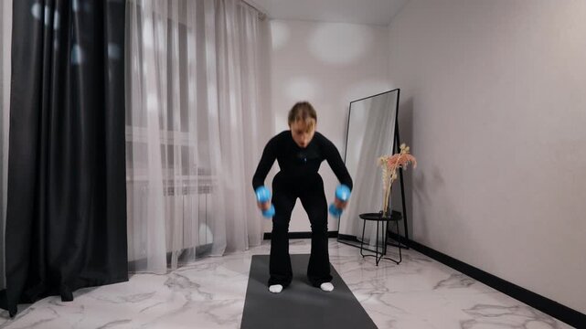 Young blonde woman in black activewear doing dumbbell deadlift during a home workout on a mat in a bright minimalist living room, front view