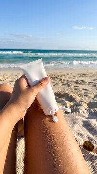 Hand Squeezing Sunscreen Tube on Tanned Leg at Beach
