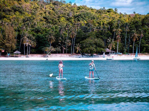 View of couple of tourist are enjoy on water sport paddle sup-board with kayaking along at the edge of the sea beach under crystal clear of water in the island of summer trip