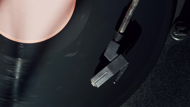 Close up of a black vinyl record rotating on a turntable while sunlight illuminates the colorful label. The footage represents vintage entertainment, music listening, and a nostalgic lifestyle.