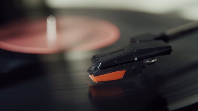 Extreme close up of a stylus resting in the groove of a rotating vinyl record while music plays on a vintage turntable in sunlight