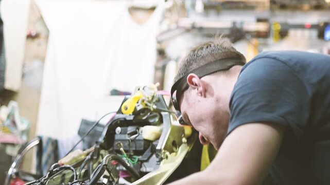 Skilled mechanic repairing a motorcycle engine in a busy workshop with headlamp