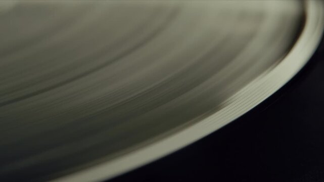 Close-up of a vinyl record playing on a turntable in the sunlight. The macro footage reveals detailed grooves and surface texture while the vintage disc rotates smoothly.