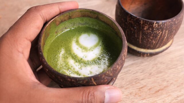 Matcha latte art in coconut shell bowl on wooden table top view closeup