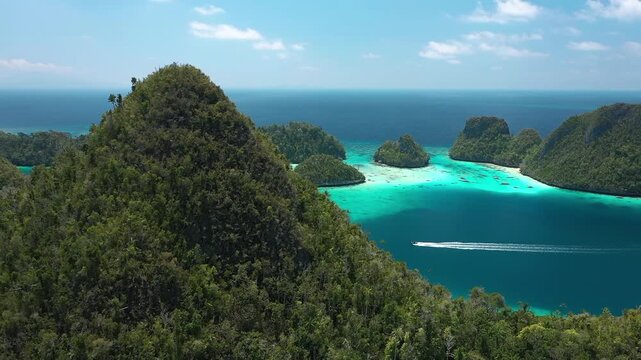 Aerial view of lush tropical islands in Raja Ampat archipelago with turquoise water and speed boat sailing.