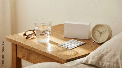 Medical pills blank box and glass of water on wooden nightstand