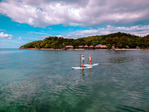 View of couple of tourist are enjoy on water sport paddle sup-board with kayaking along at the edge of the sea beach under crystal clear of water in the island of summer trip
