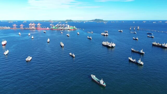 Fleet of oil tanker ships and commercial cargo vessels anchored in the deep blue sea near a long bridge. Global maritime logistics, international shipping trade, and energy transport.	