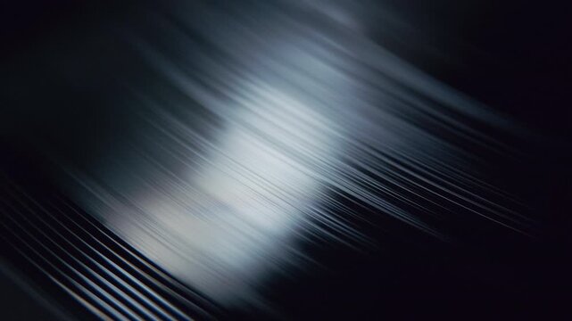 Extreme close up of a black vinyl record spinning under reflected light, revealing the intricate texture of its grooves. The footage creates an abstract visual of analog music media