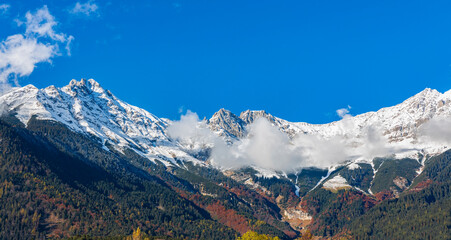 Obraz premium The landscape view of Snow-Capped Mountain Peaks and forest autumn trees scene background under a Clear Blue Sky
