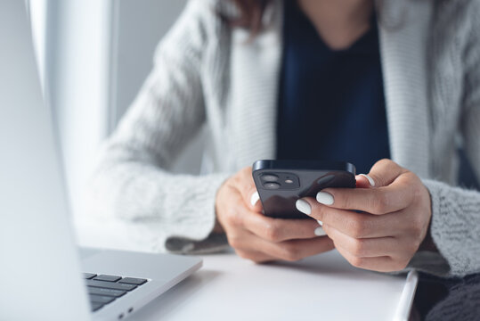 Business woman using smartphone with laptop on office desk, surfing the net, searching the information at office, close up