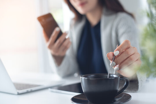 Business woman using mobile phone during working on laptop, with cup of coffee on office desk, closeup, people lifestyle, taking a coffee break