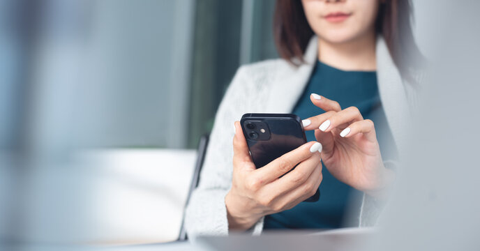 Asian business woman using mobile phone during working on laptop, surfing the internet, searching the information at office.