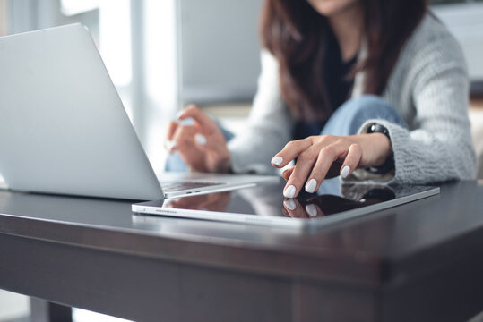 Woman in casual clothing sitting on the floor working on laptop and using digital tablet at home office, remote work, online business concept