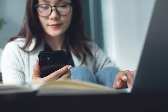 Asian business woman using mobile phone during working on laptop at home office, remote work concept