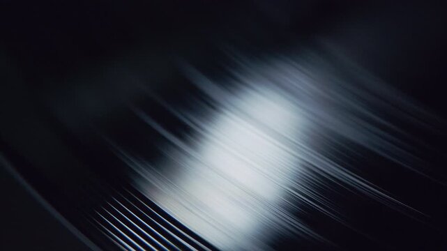 Detailed macro shot of rotating vinyl grooves with light reflections moving across the dark surface. The scene highlights the texture, shine, and mechanical beauty of a classic music recording medium