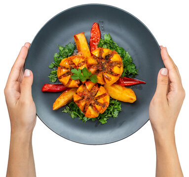 Top view of hands holding a dark plate with baked stuffed potatoes and roasted peppers, isolated on transparent background.