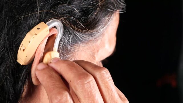 Close-up of senior person putting on and adjusting a hearing aid, demonstrating the use of this assistive device for better hearing
