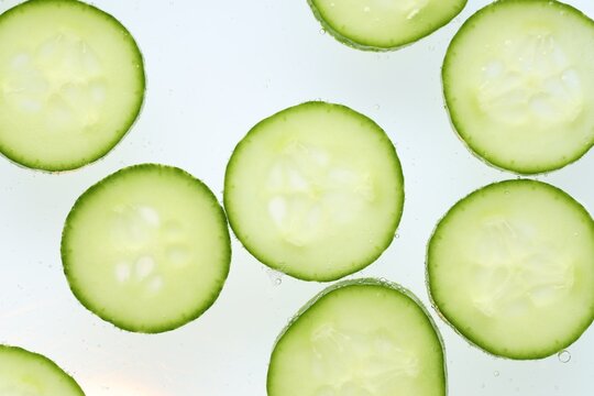 Slices of cucumber in water against white background