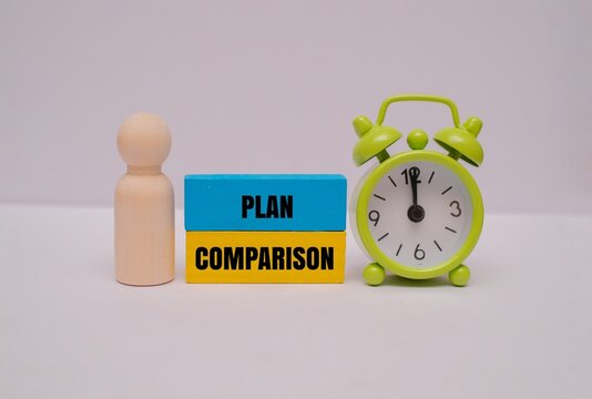 Wooden figure standing next to "PLAN COMPARISON" text blocks and alarm clock. Representing time management, options evaluation, and strategy