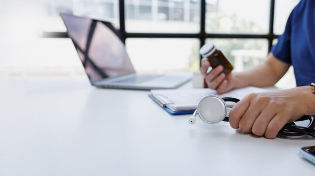 Healthcare professional reviewing patient information and medical prescriptions while holding a stethoscope and medication bottle in a clinic office
