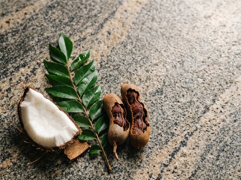 Coconut half, tamarind pods and green leaf on stone countertop