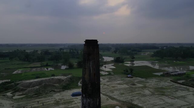 Close up aerial view of brick kiln chimney against rural landscape at sunset, drone footage