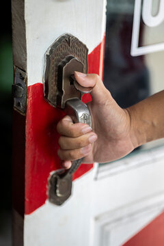 Close-up of a hand opening a vintage door handle at the entrance of a barbershop.