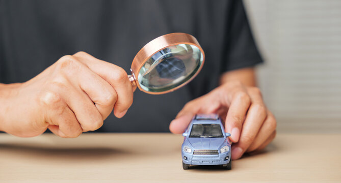 A hand holds a magnifying glass inspecting a toy car, symbolizing vehicle search, repair check, or insurance evaluation. Highlights automotive service needs and financial planning