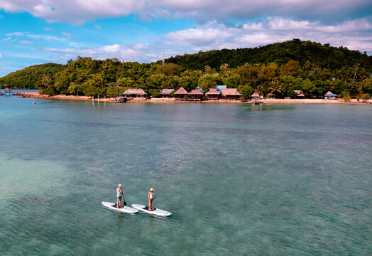 View of couple of tourist are enjoy on water sport paddle sup-board with kayaking along at the edge of the sea beach under crystal clear of water in the island of summer trip
