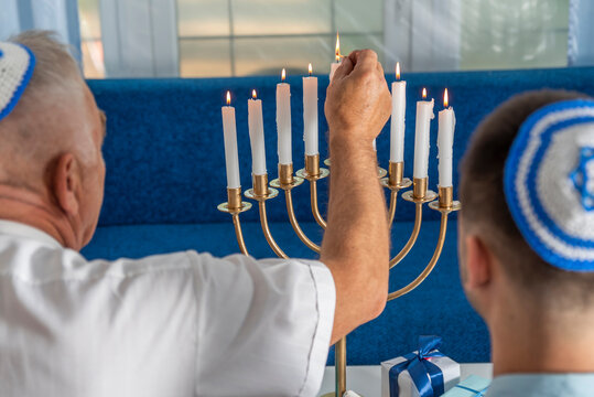 Hanukkah holiday. A senior man and young guy wear kippahs on heads in front of Jewish Hanukkah Menorah, lighting fire of candles. Yarmulke with Star of David. Traditional Hebrew Festival of Lights