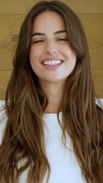 Charming brunette woman with long, beautiful, wavy hair smiling genuinely and looking directly at the camera, showing a happy and positive emotion with perfect white teeth and healthy skin
