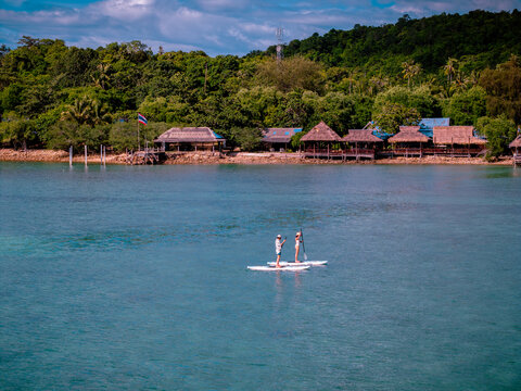 View of couple of tourist are enjoy on water sport paddle sup-board with kayaking along at the edge of the sea beach under crystal clear of water in the island of summer trip