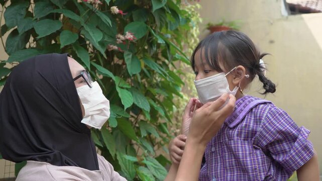 Asian mother adjusting face mask on her young daughter