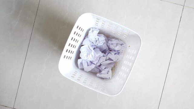 Crumpled paper balls tossed into white trash bin on tiled floor with shadow