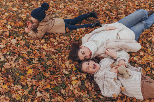 Happy mother and two children lying on ground covered with vibrant autumn leaves in park.Joyful family moment during autumn season. Love, family lifestyle, happiness, connection with nature.
