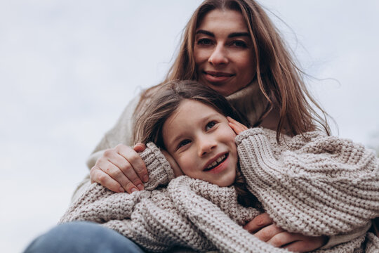 Close-up portrait of mother and daughter wearing cozy knitted sweaters. Family love, motherhood, bonding, comfort, happiness, tenderness, fashion, togetherness, warmth, authentic lifestyle.