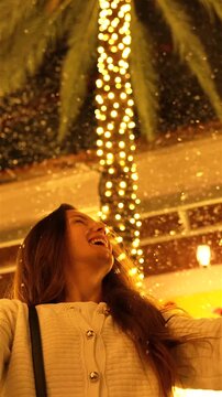 Joyful woman raising hands under a Christmas-lit palm tree