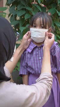 Asian mother adjusting face mask on her young daughter