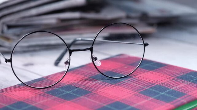 Pair of round black glasses resting on red checkered notebook surface with blurred background