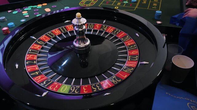 Casino roulette wheel under bright indoor light with hands, chips, and numbered betting ring surrounding glossy black table for tense gambling action and lively gaming atmosphere
