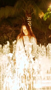 Smiling woman in a glowing fountain among festive palm trees