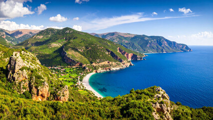 Obraz premium Scenic coastal landscape with turquoise sea, green mountains, and blue sky on a sunny day